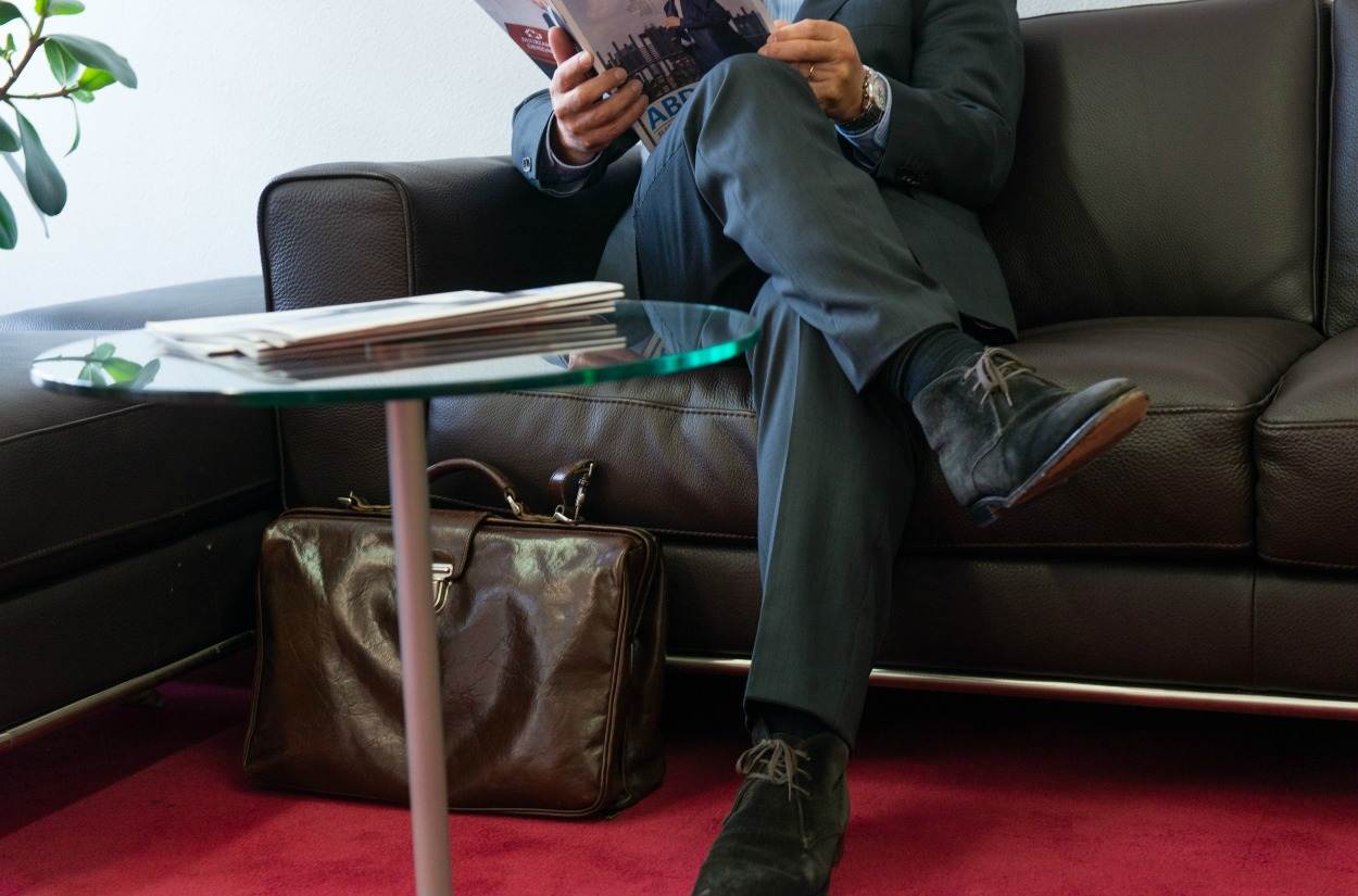 Man met aktetas die een magazine leest op een bank